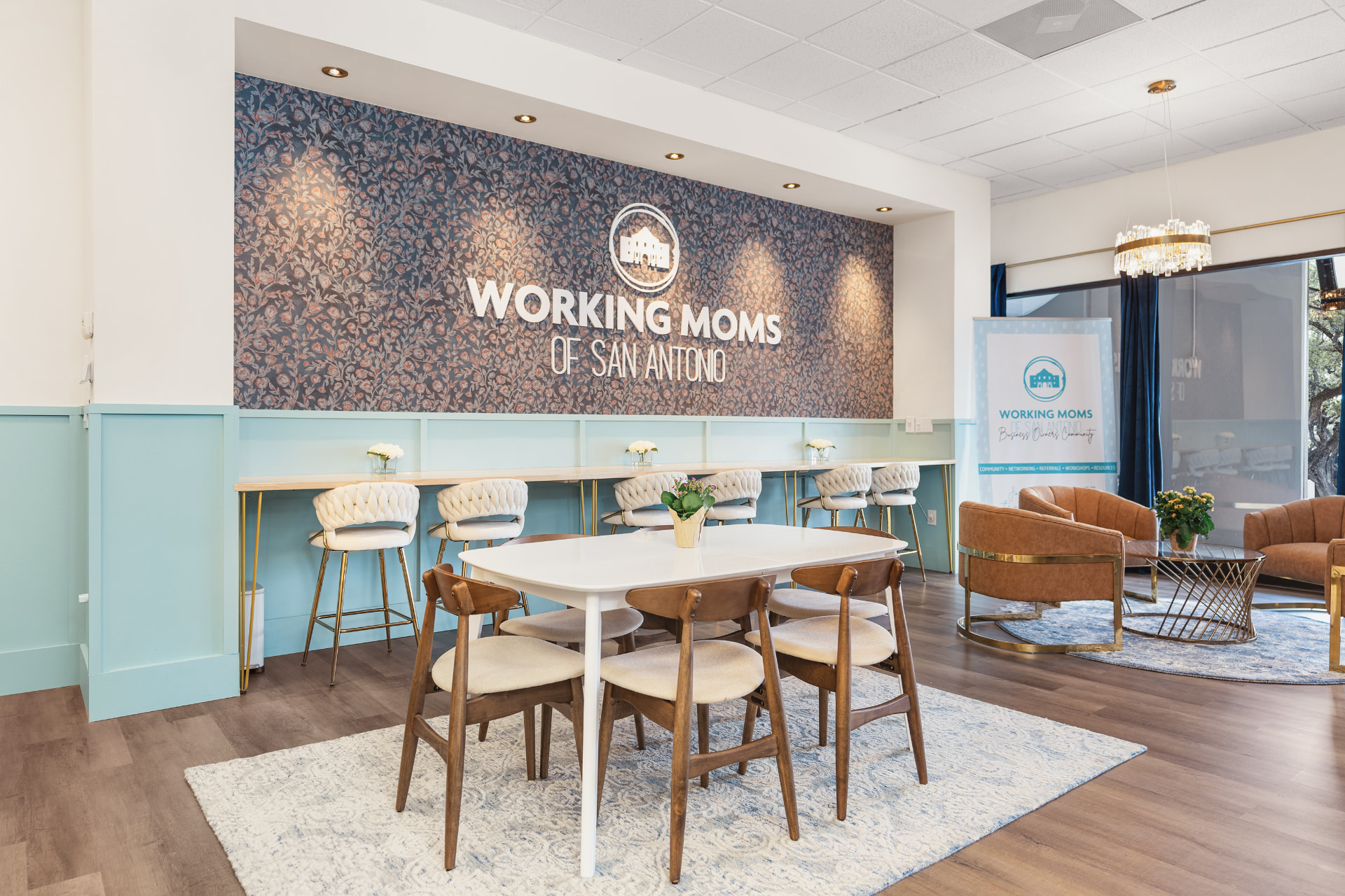 The Working Moms of San Antonio community space with the WMSA logo wall, high-top seating, and a warm meeting area